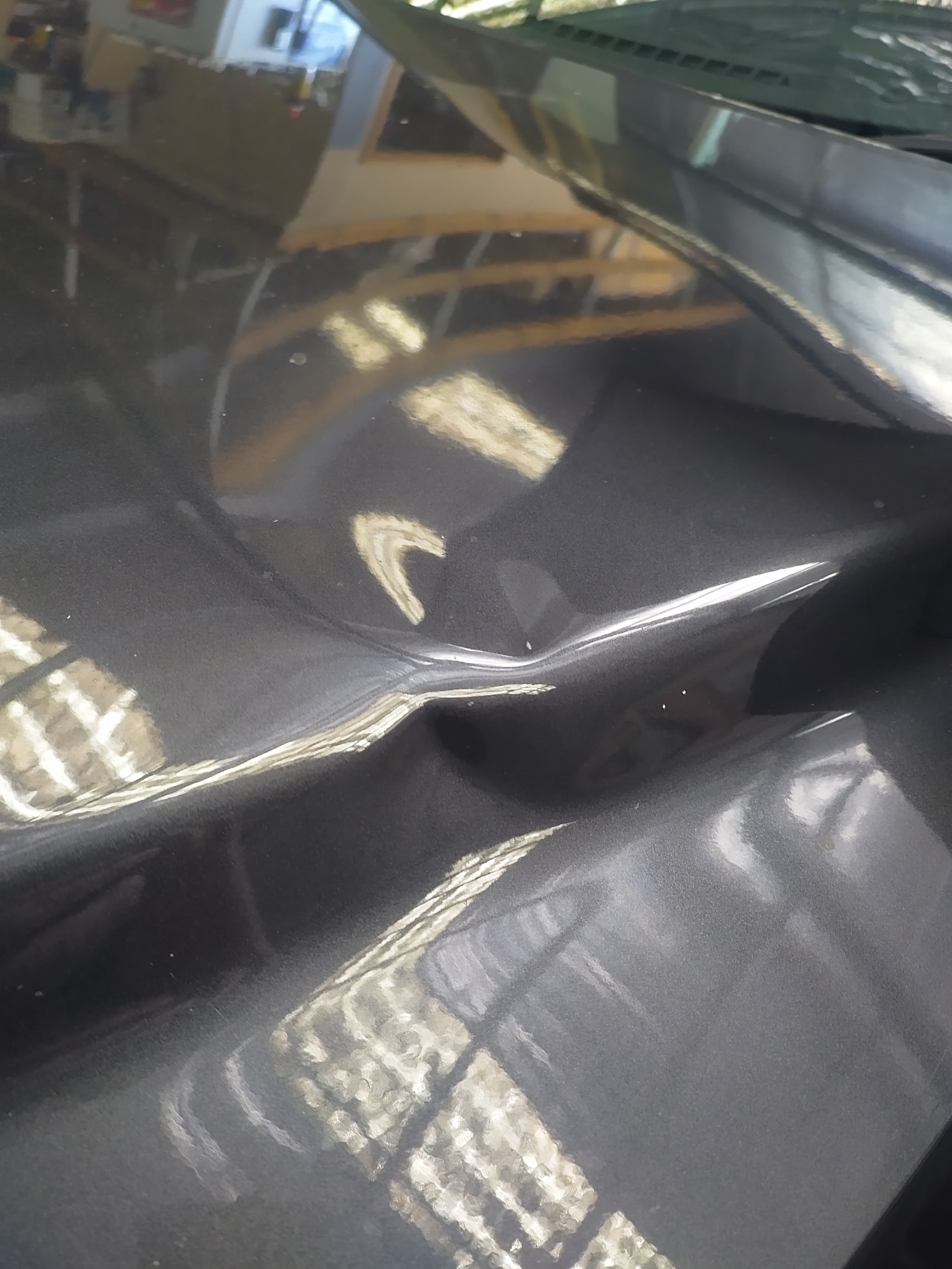 A dent in a dark panel, the reflection bending where the metal is pushed in