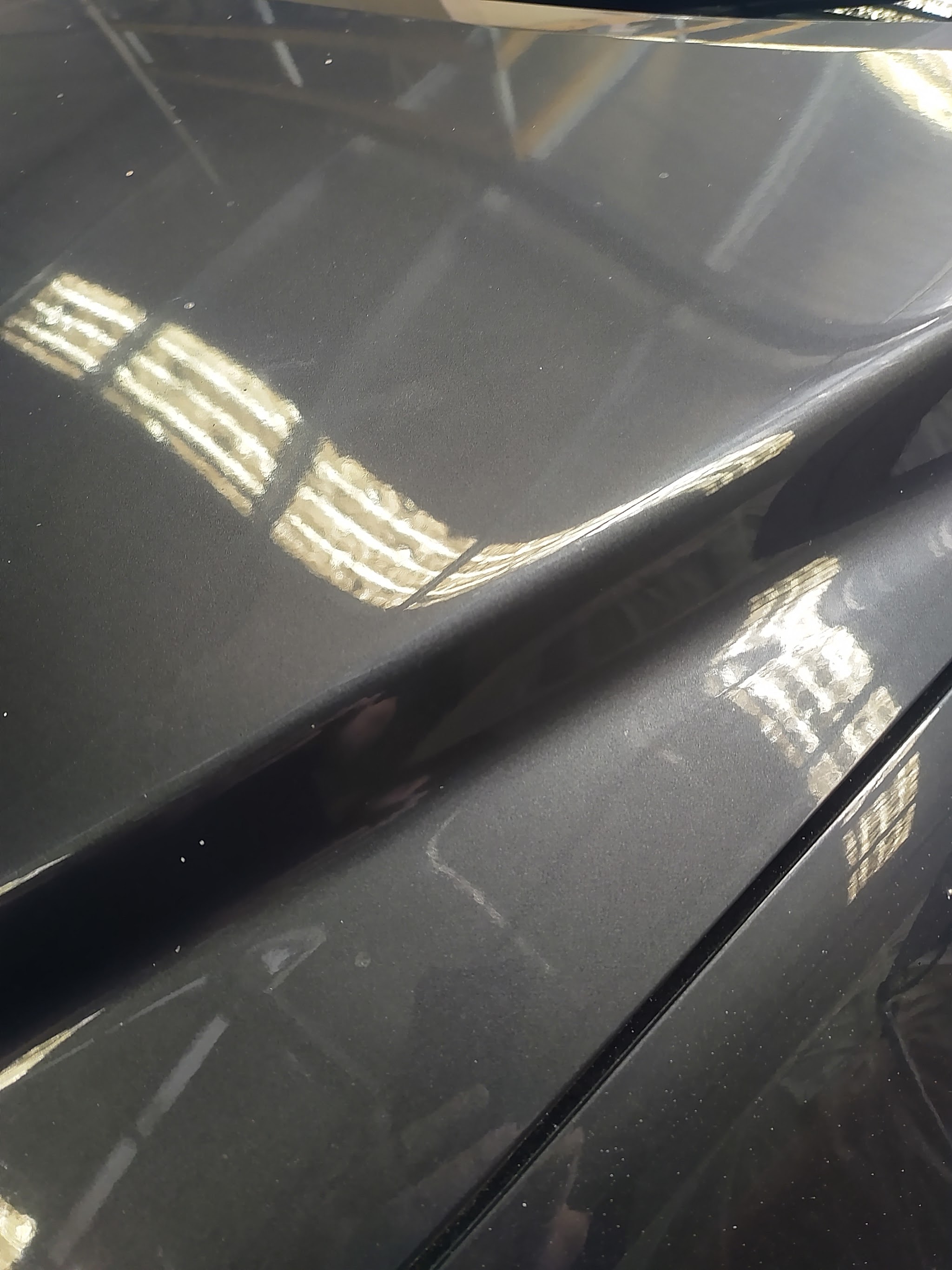Close-up of a sharp crease in a dark grey panel with workshop lights reflecting in it