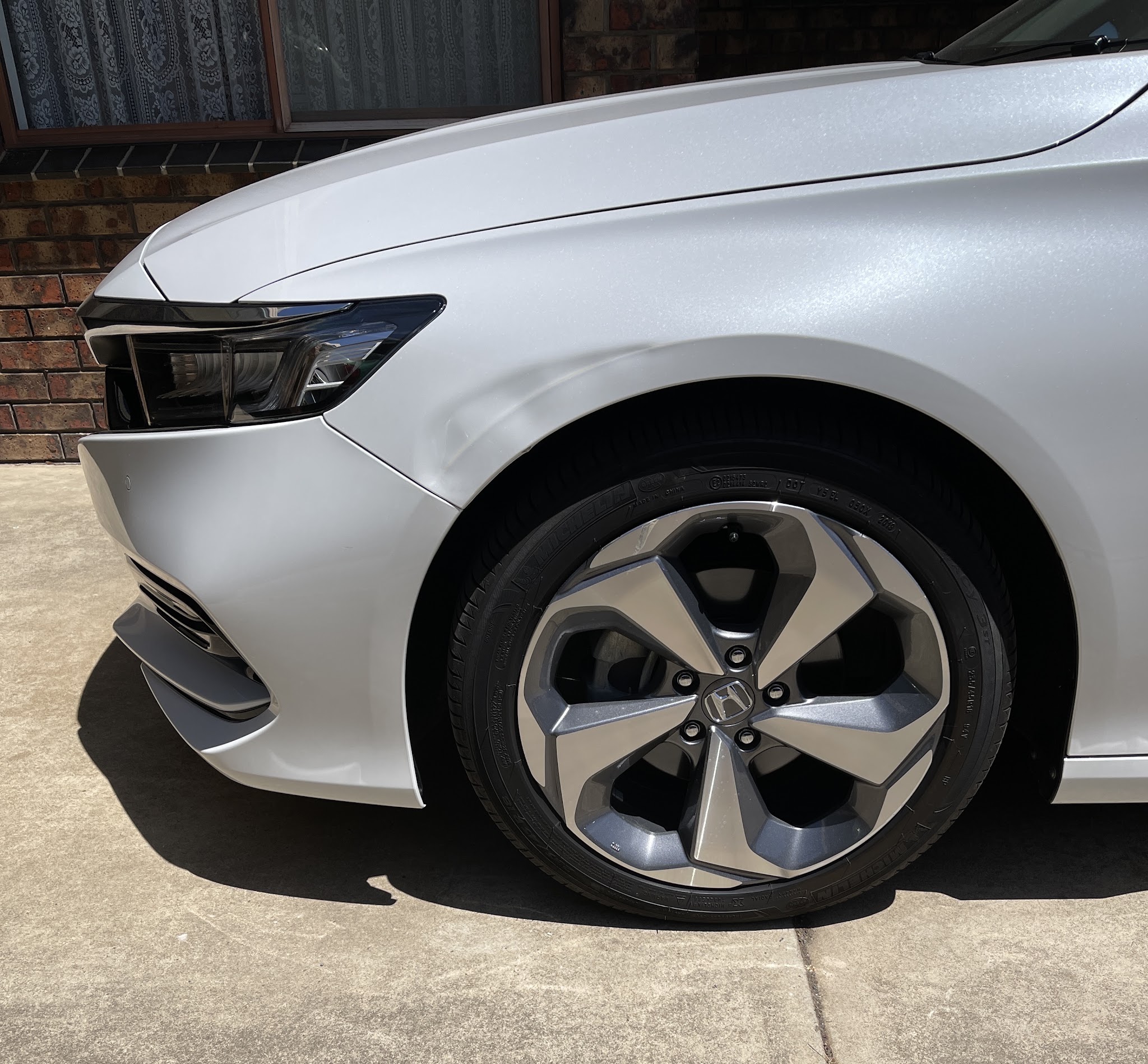 White Honda with a sharp crease along the front guard above the wheel